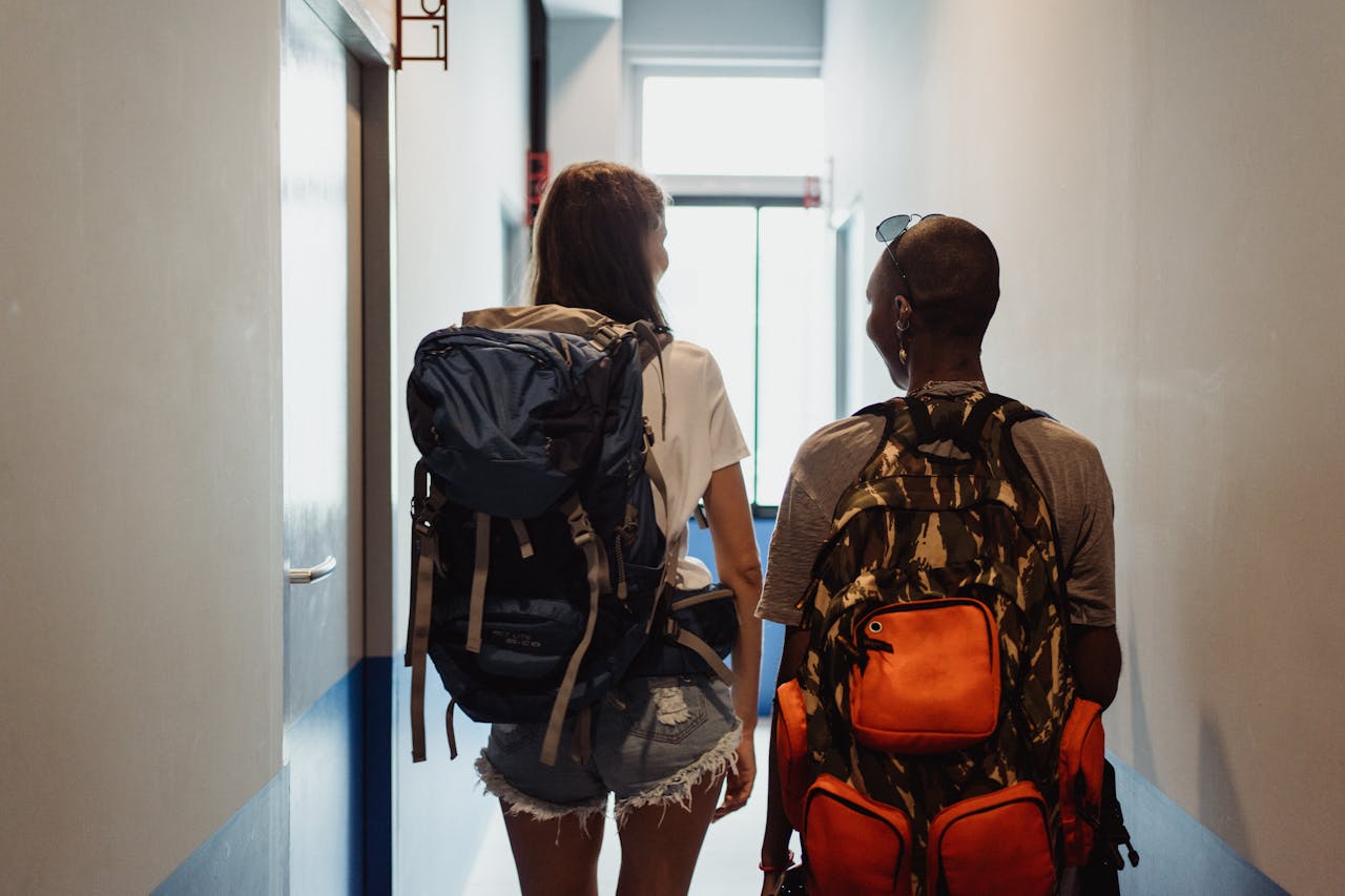 Two friends walking in a hostel corridor with backpacks, embodying travel and adventure vibes.