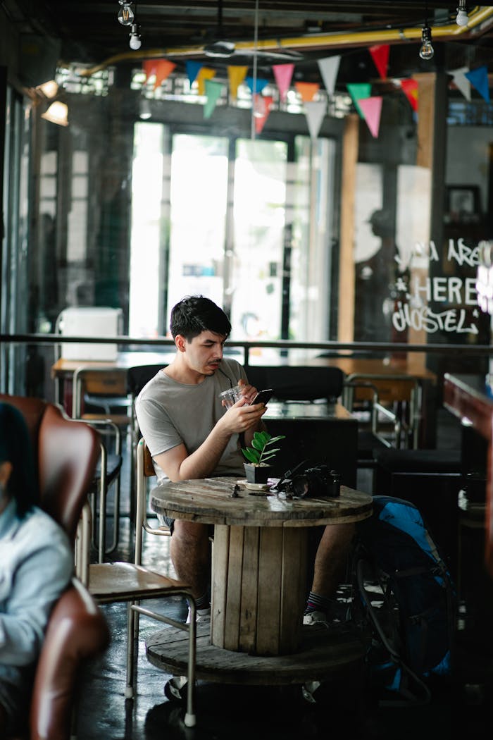 Casual setting of a young man focused on his phone in a rustic cafe.